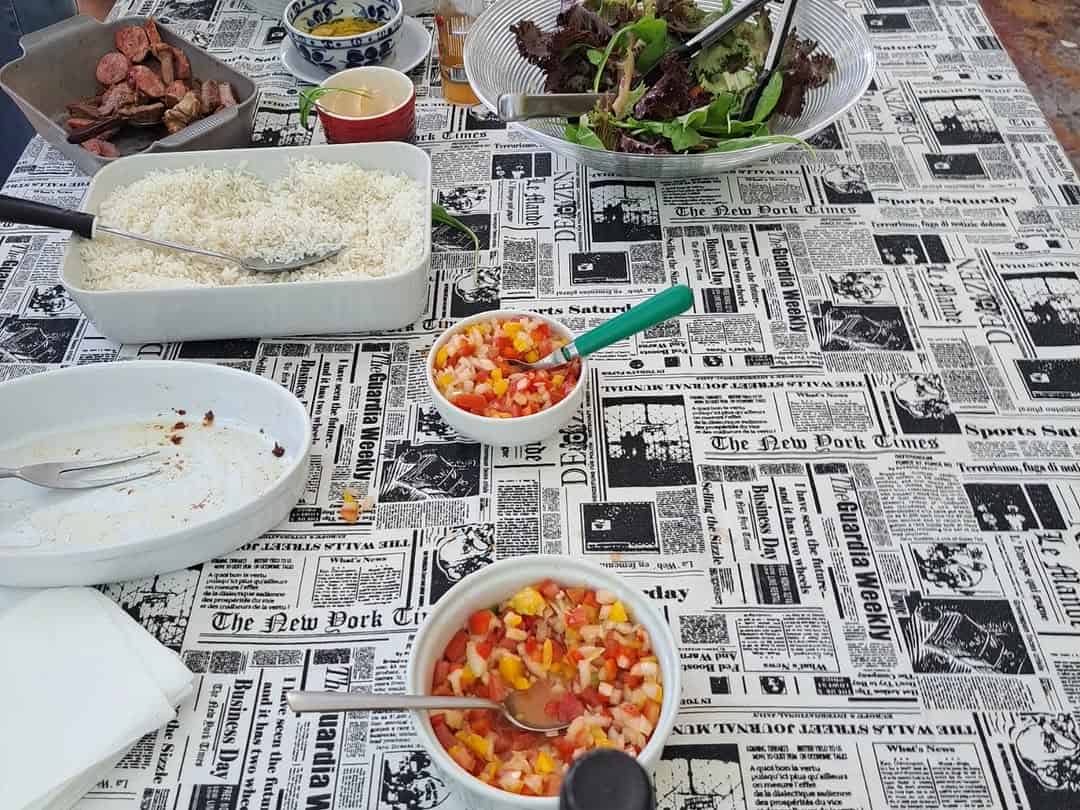 20251130-142351-1-6 Bolinhos de carne e salada em taças, pratos de comida com coberturas coloridas, mesa com pratos e talheres, fundo de jornal antigo.