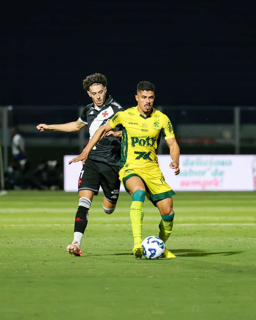 Atleta usando uniforme amarelo tenta controlar a bola, enquanto adversário de uniforme preto tenta interceptar.