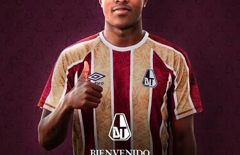 Jogador do Vasco com uniforme oficial, mostrando o escudo e detalhes do time em fundo roxo.