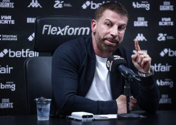 Futebolista do Vasco em entrevista; fundo com logos de patrocinadores.