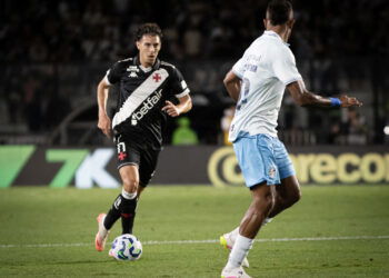 Jovem jogador com uniforme preto, correndo com a bola em campo.
