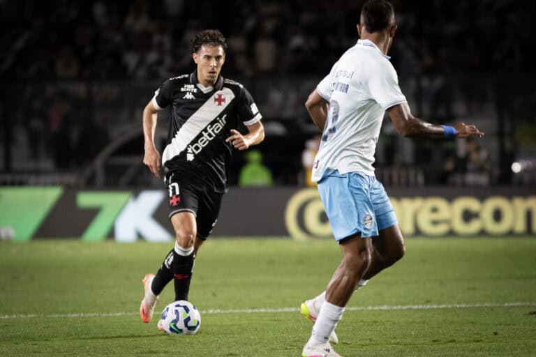 Jovem jogador com uniforme preto, correndo com a bola em campo.