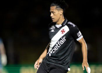 Camisa do Vasco, jogador em campo com uniforme preto e branco, estádio vazio ao fundo.