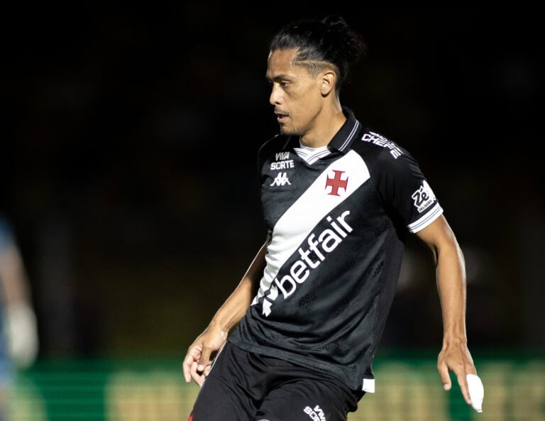 Camisa do Vasco, jogador em campo com uniforme preto e branco, estádio vazio ao fundo.