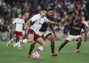 Jugador de futebol batalhando pela bola com adversário em campo.