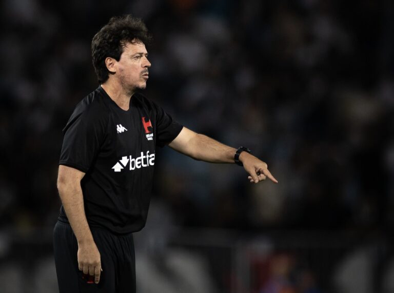 Imagem de homem técnico de futebol vestindo camisa preta, apontando com o braço estendido.