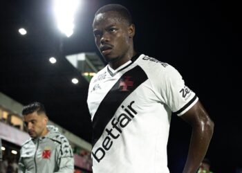 Jogador do Vasco usando uniforme branco com detalhes pretos e logotipo vermelho na camisa.