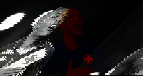 Atacante do Vasco comemorando gol com a camisa do time, com fundo escuro e iluminação focada, expressando alegria e entusiasmo na partida.