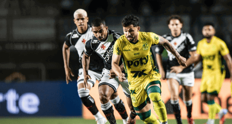 Alt: Jogadores do Vasco e adversários disputam a bola em jogo de futebol profissional.