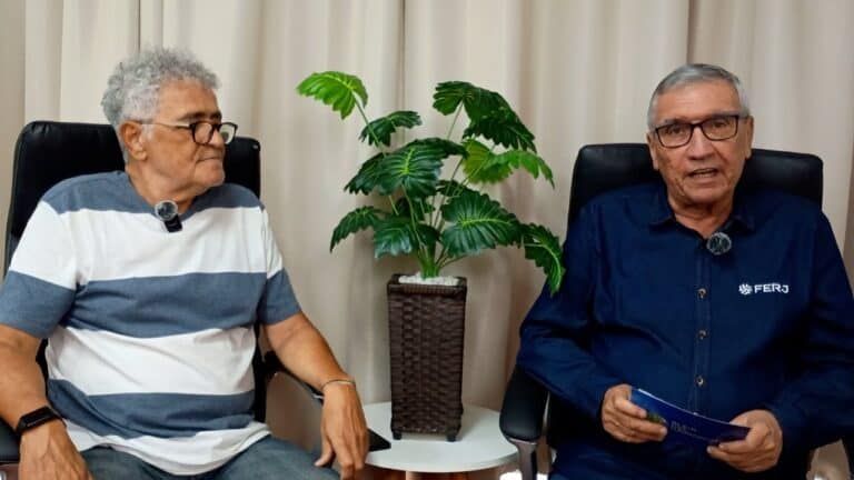 Homens conversando em ambiente interno com planta ao centro.