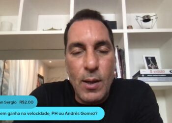 Homem falando em vídeo, fundo com estante e livros.