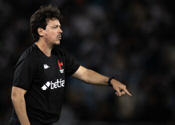 Árbitro no campo apontando, vestindo uniforme preto com logo do clube.