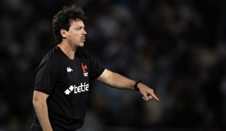 Árbitro no campo apontando, vestindo uniforme preto com logo do clube.